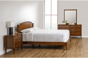 A well-lit, spacious bedroom featuring the Toulon bedroom set, including a sleek wooden bed with a high headboard, a matching nightstand with three drawers to the left, and a wide dresser with multiple drawers to the right, all in a rich, warm wood tone. 