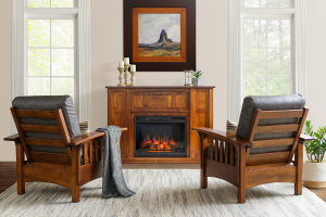A cozy living room featuring two Mission style wooden chairs with dark leather cushions flanking a fireplace, atop a textured area rug. The room is brightened by natural light from two large windows, and decorated with a painting above the mantelpiece, ac